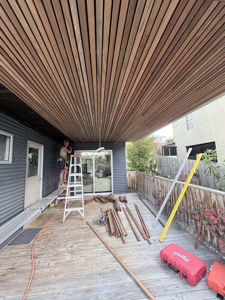 Hardwood batten ceiling going up over a covered deck, carpenter on a ladder at the far end