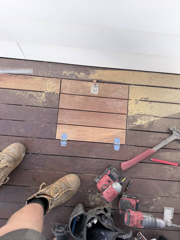 Hinged access hatch cut into a hardwood deck, with a recessed ring pull and stainless hinges