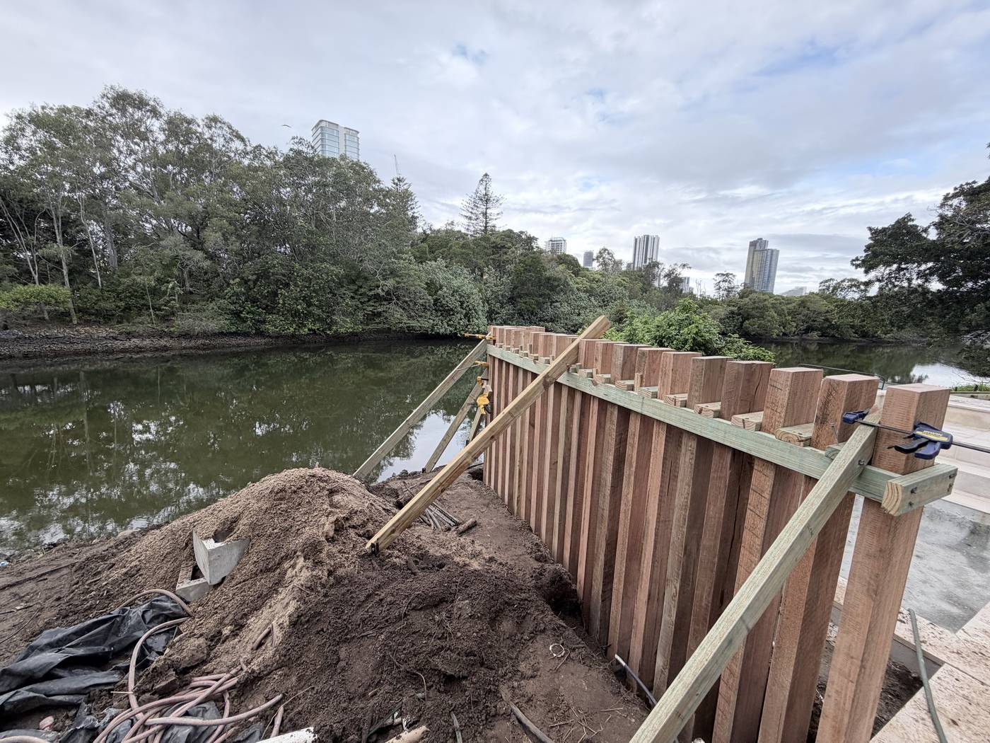 Rough-sawn hardwood pool screen going up on a riverfront block, battens set off a spacer jig