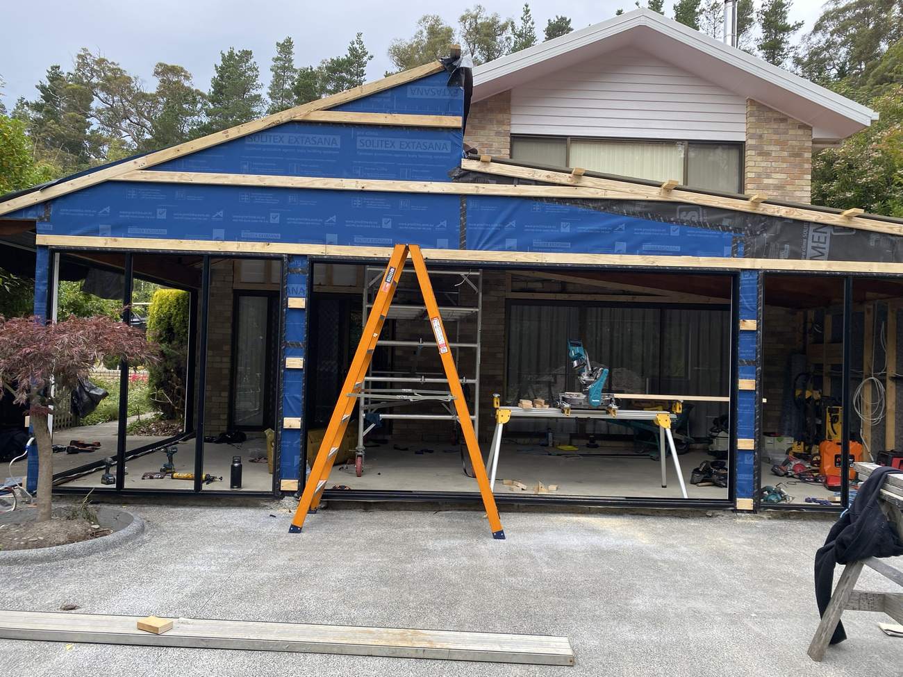 New black-framed windows and sliding doors installed, walls wrapped and taped